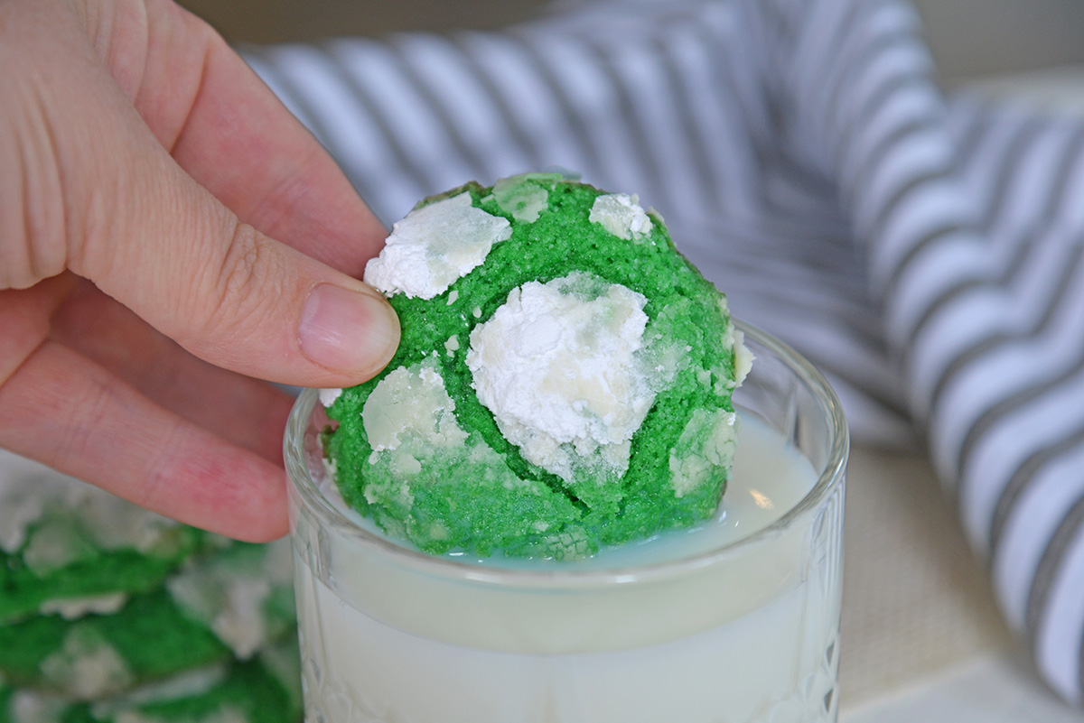 straight on shot of green mint crinkle cookie dipped into glass of milk