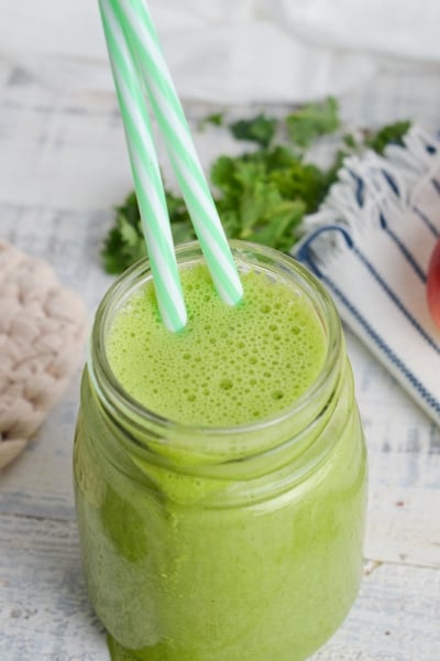 angled shot of green smoothie with two straws