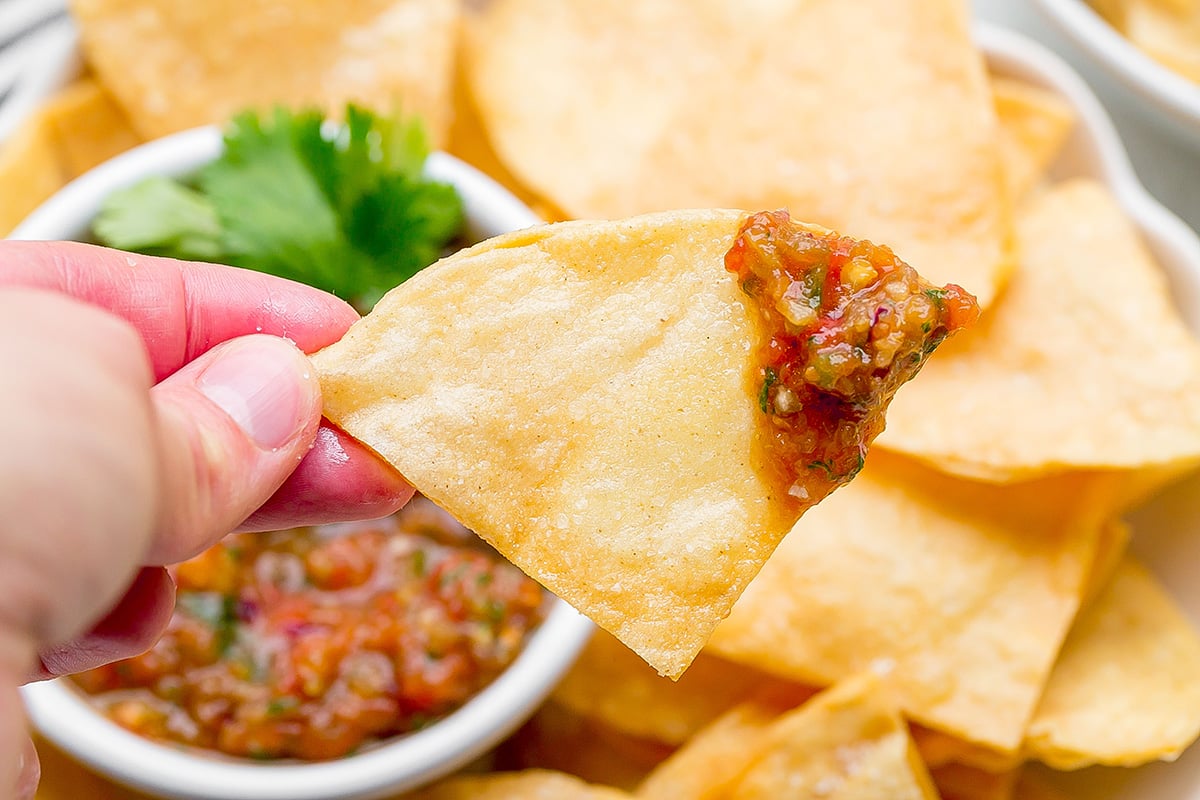 close up of hand holding tortilla chip dipped in salsa