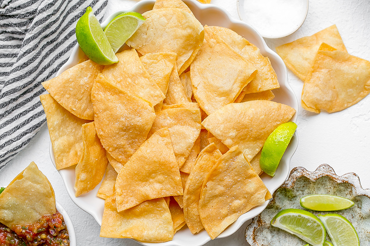 overhead shot of bowl of tortilla chips with lime wedges