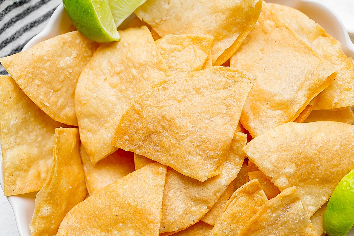 close up overhead shot of bowl of tortilla chips with lime wedges