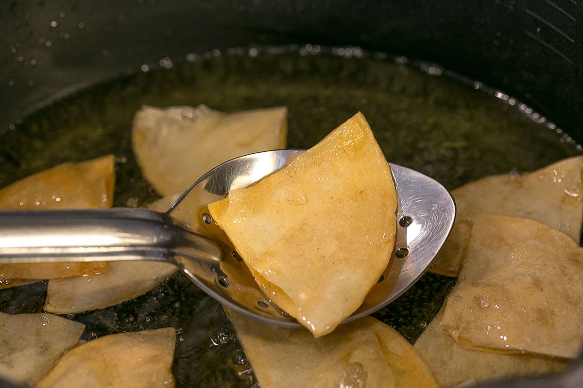 angled shot of tortilla chip coming out of oil on slotted spoon
