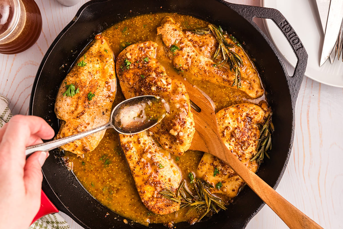 spoon basting chicken in honey mustard sauce