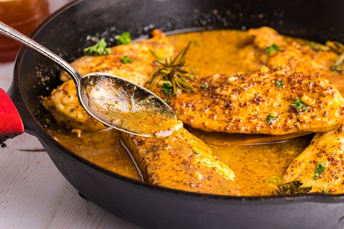 angled shot of spoon basting chicken in pan