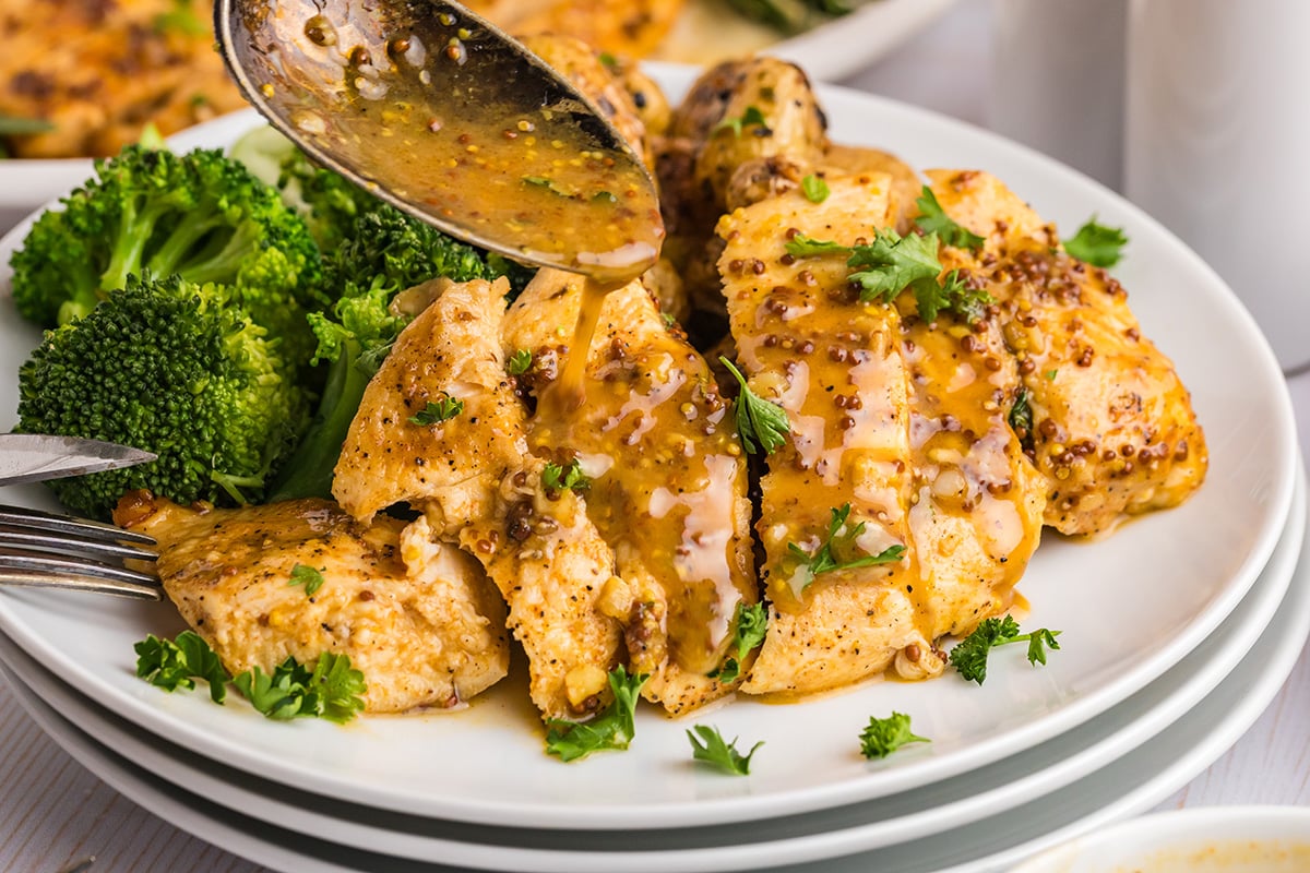 angled shot of spoon adding sauce to sliced chicken