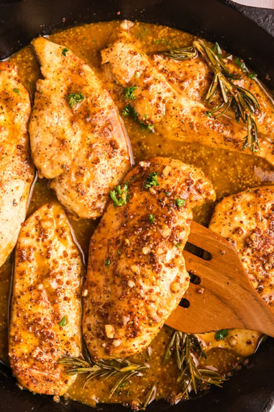 overhead shot of wooden spoon in skillet of honey mustard chicken