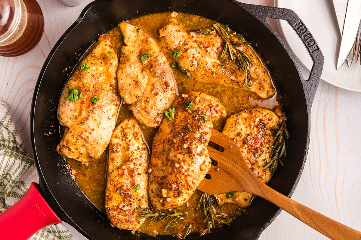 overhead shot of wooden spoon in skillet of honey mustard chicken