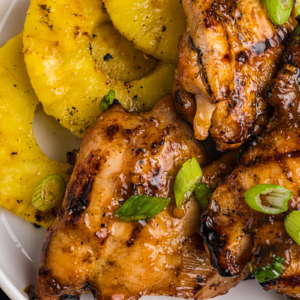 close up overhead shot of huli huli chicken and pineapple on plate