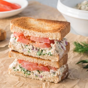 angled shot of stack of tuna salad sandwich halves on parchment paper