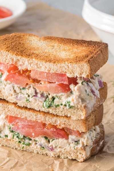 angled shot of stack of tuna salad sandwich halves on parchment paper