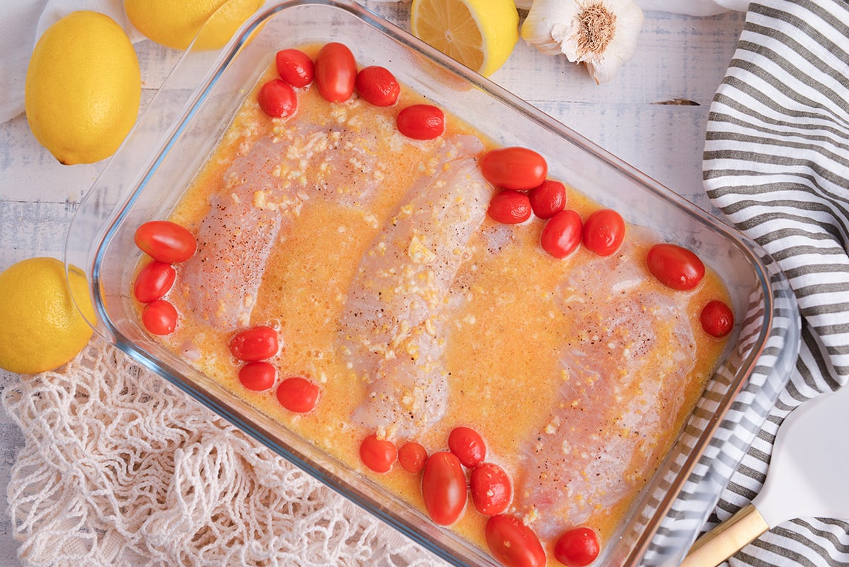 tilapia and tomatoes in baking dish topped with garlic butter