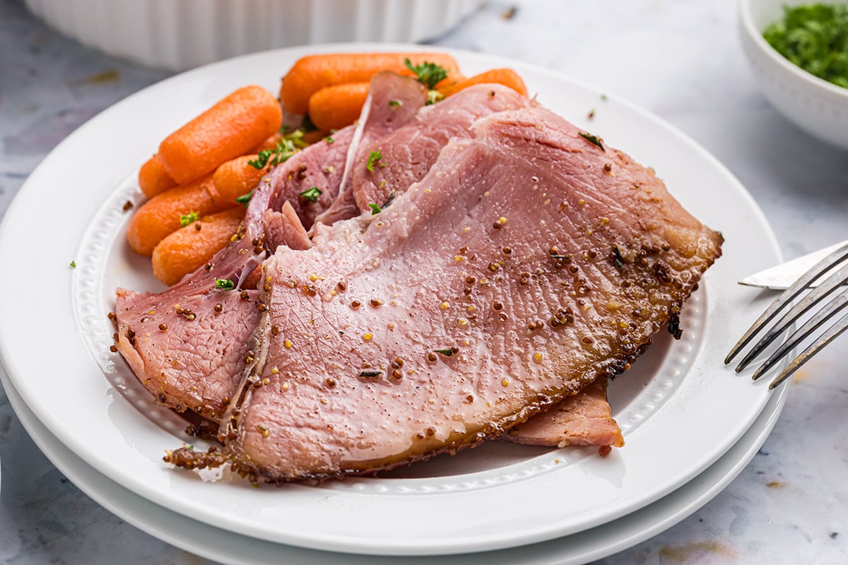 close up angled shot of plate of mustard brown sugar ham with carrots