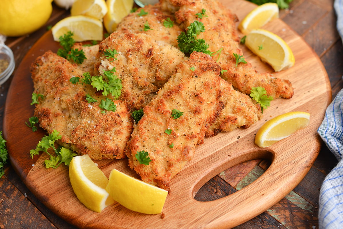 angled shot of baked caesar chicken on wooden tray with lemons