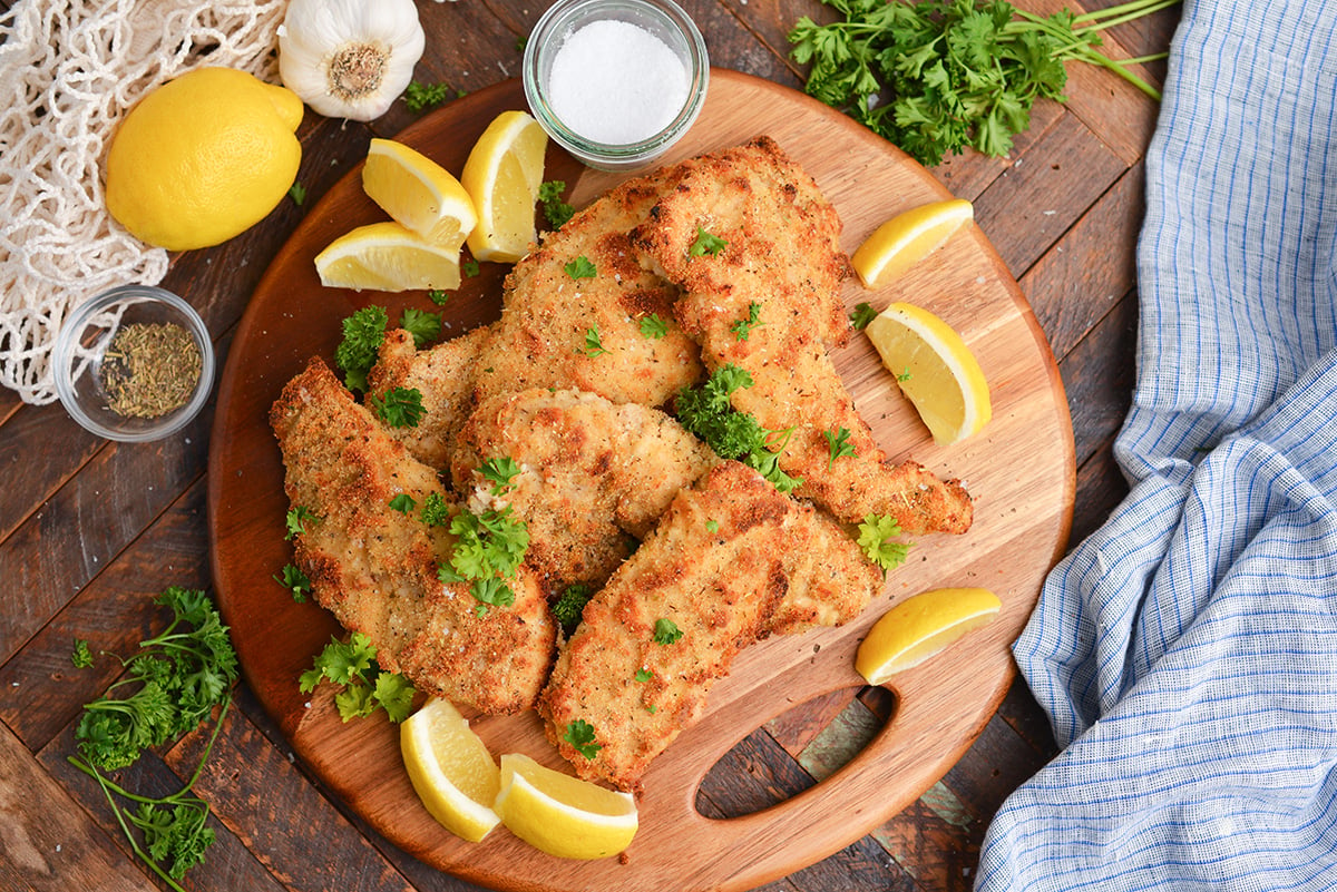 overhead shot of platter of baked caesar chicken with lemon wedges