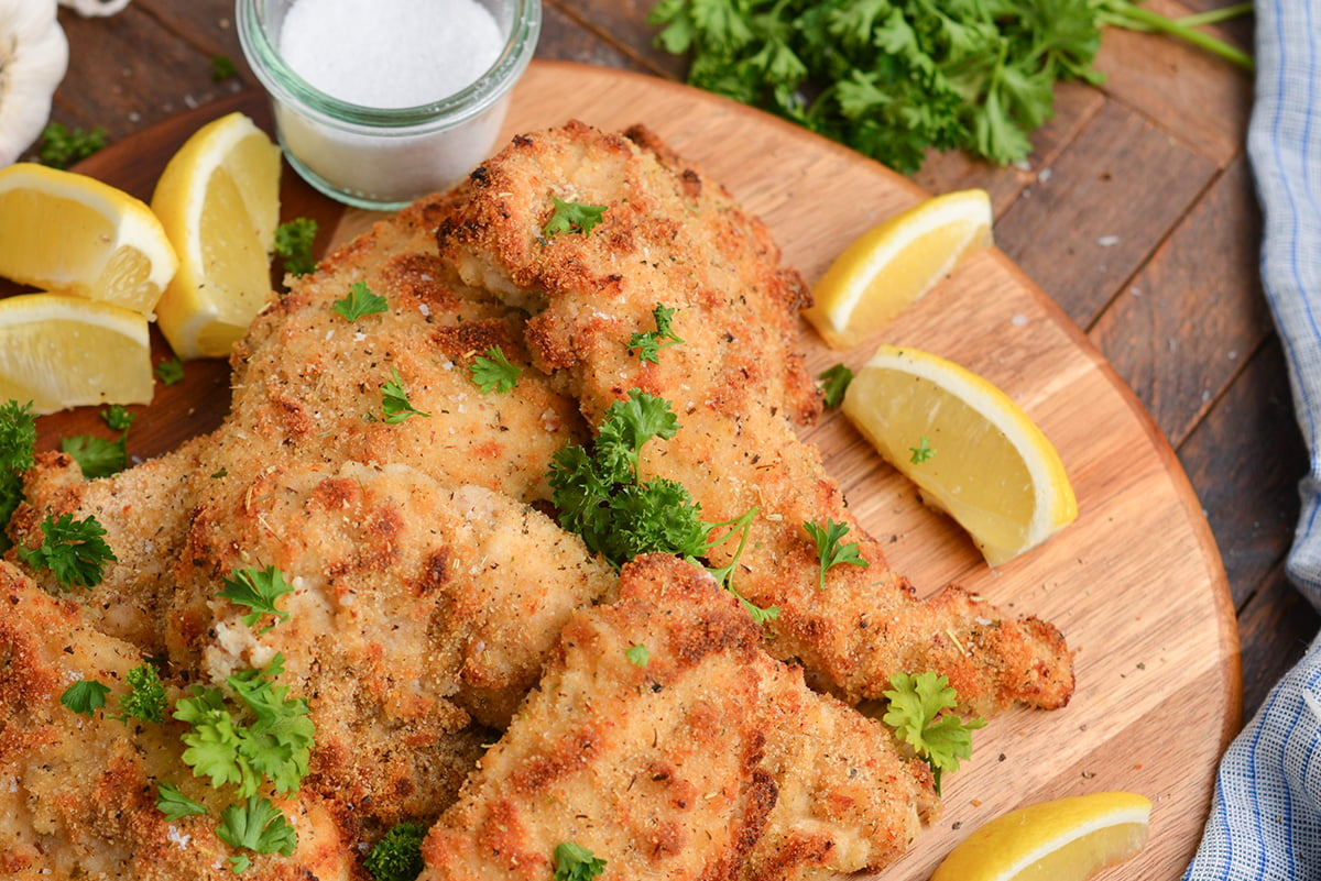 angled shot of platter of baked caesar chicken with lemon wedges