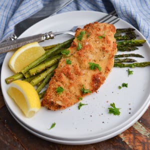 angled shot of baked caesar chicken over asparagus on plate