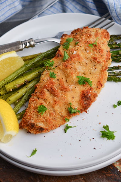 angled shot of baked caesar chicken over asparagus on plate