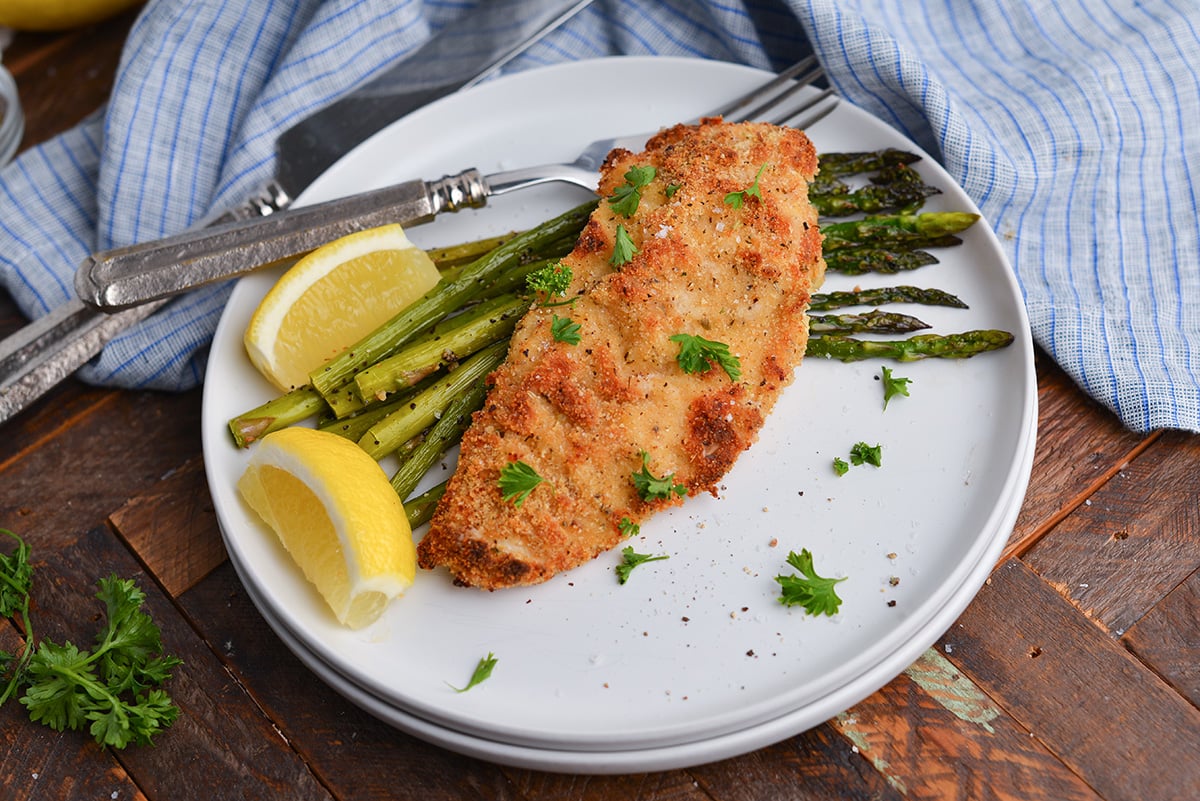 angled shot of baked caesar chicken over asparagus on plate