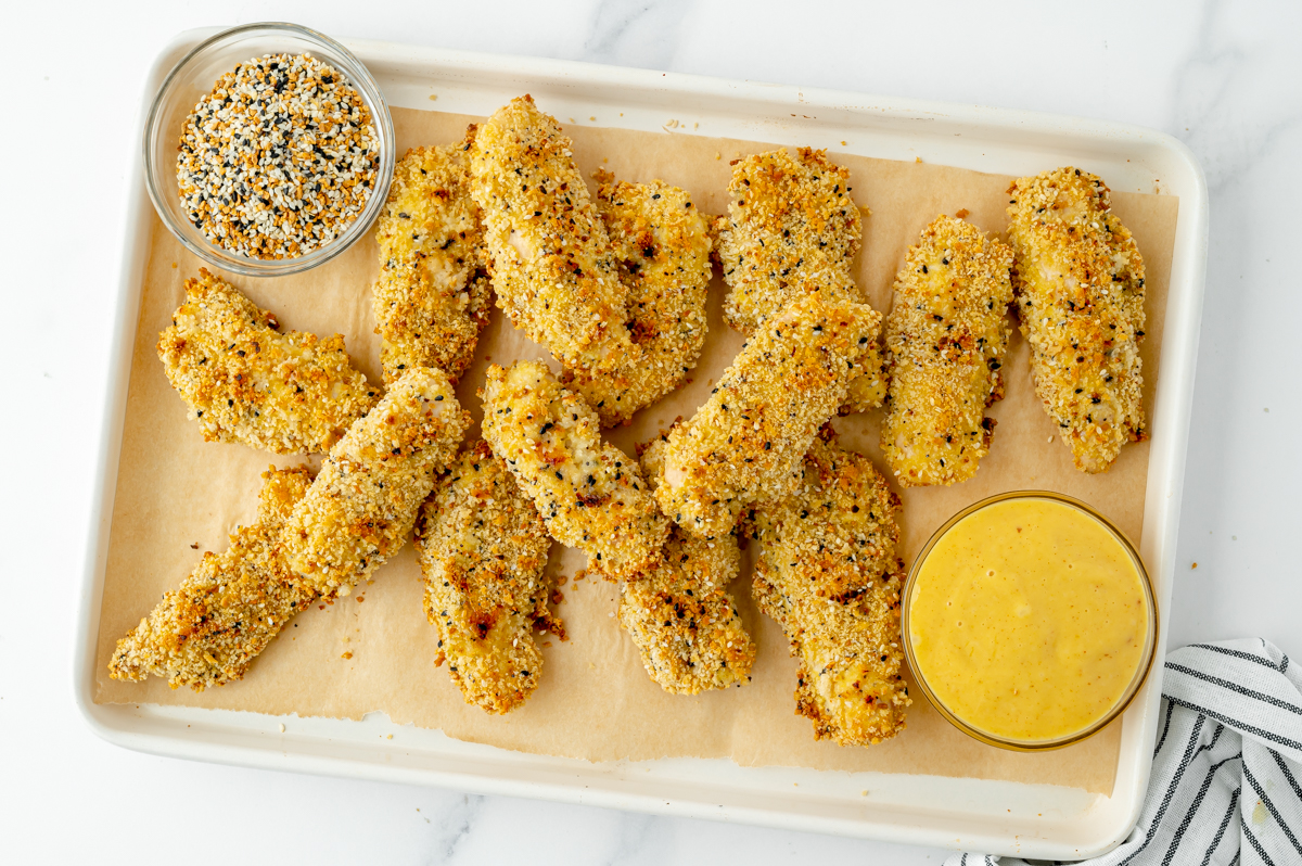 overhead shot of everything seasoning chicken tenders on sheet pan with honey mustard