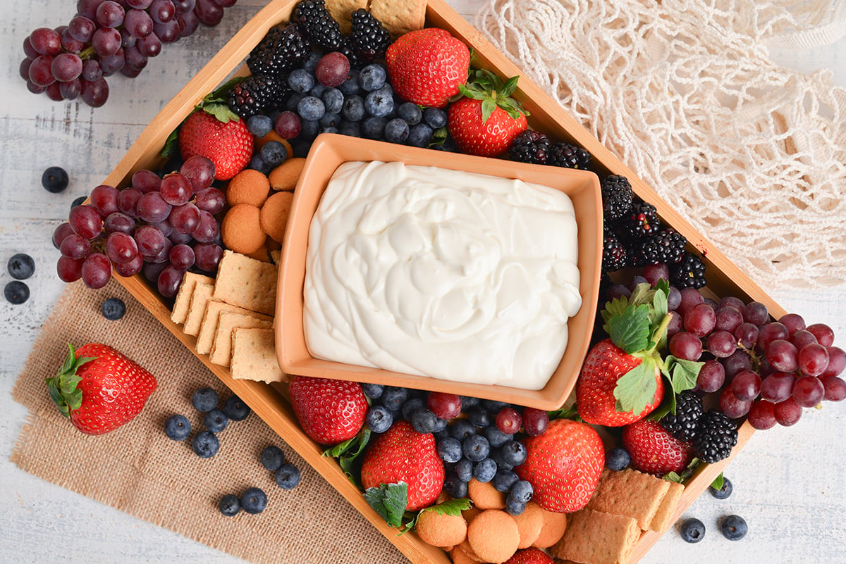 marshmallow fruit dip in a serving bowl with fresh fruit on a wood tray