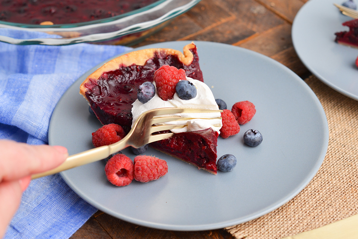 angled shot of fork digging into slice of mixed berry pie