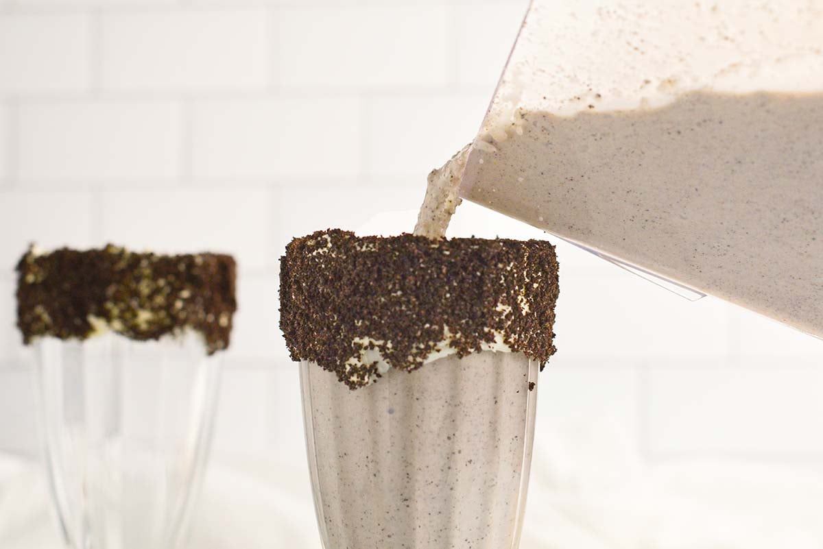 pouring milkshake into a rimmed malt glass