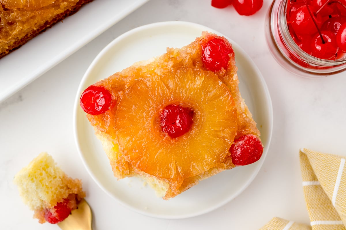 overhead slice of cake with one bite taken out, cherries and pineapples