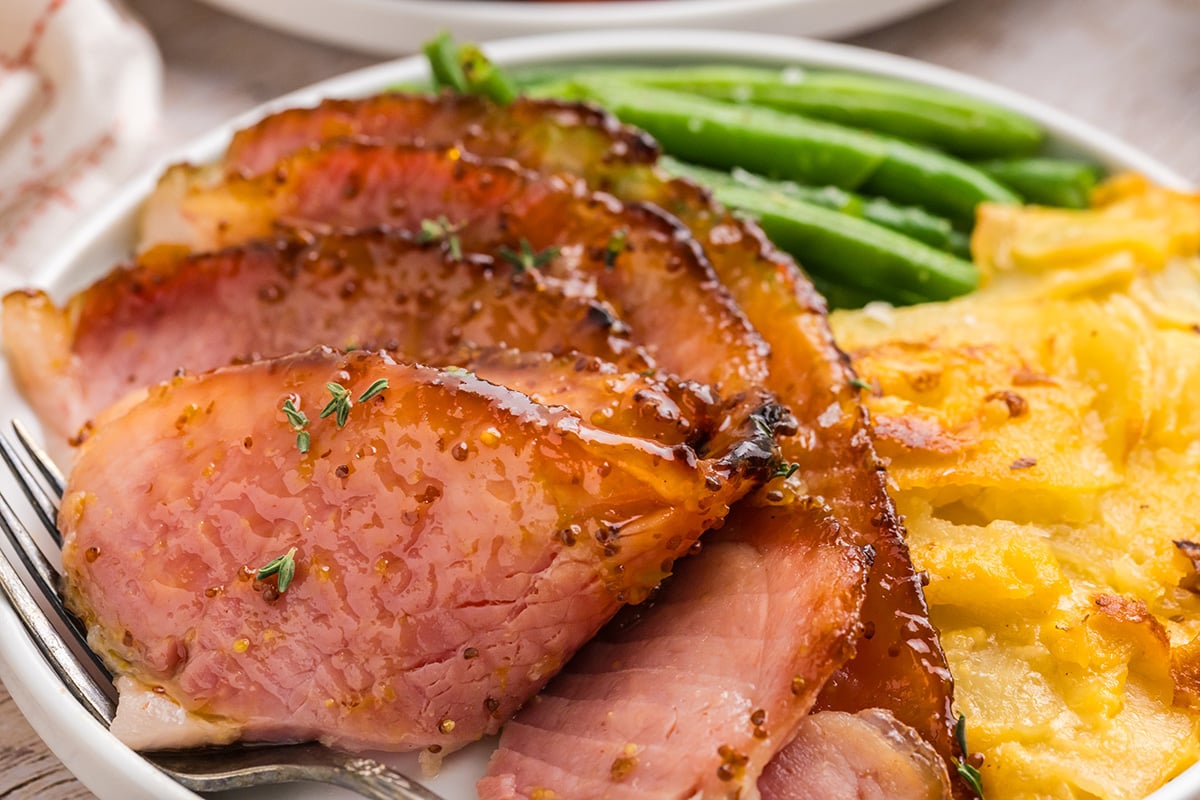 close up angled shot of sliced ham on plate with veggies