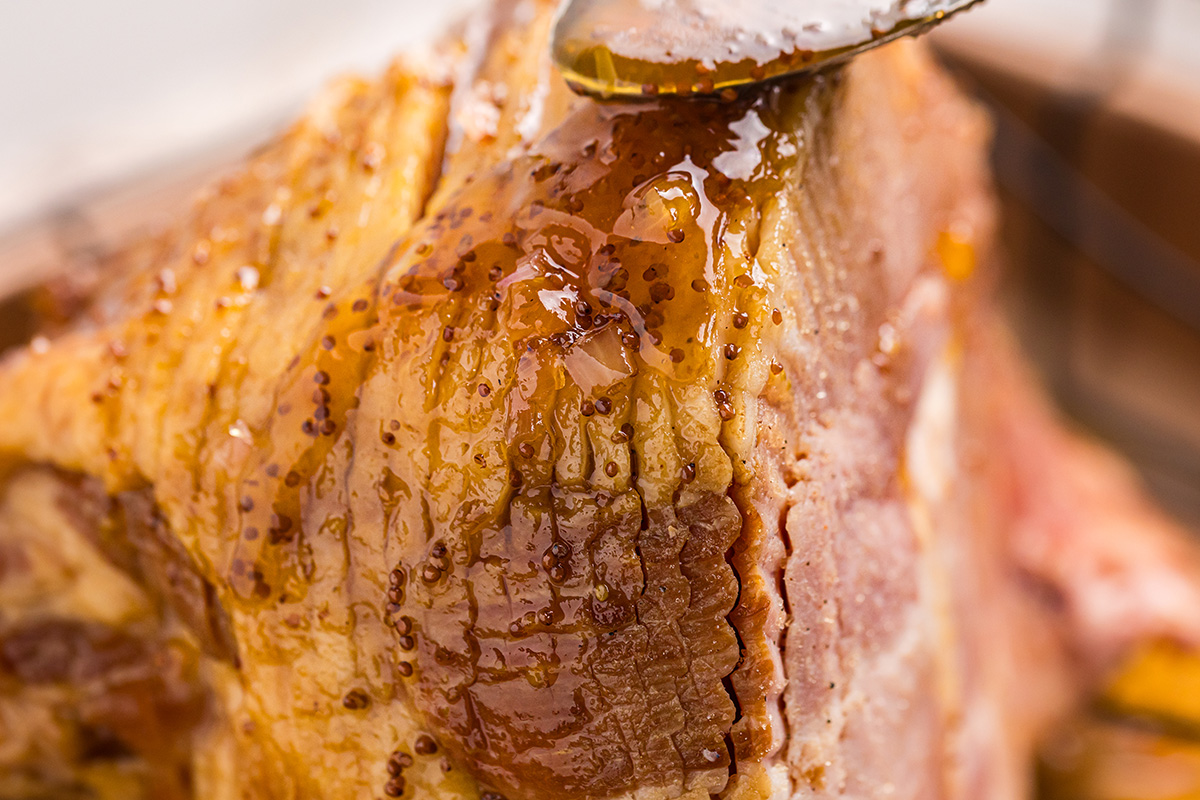 close up of spoon adding glaze to sliced ham