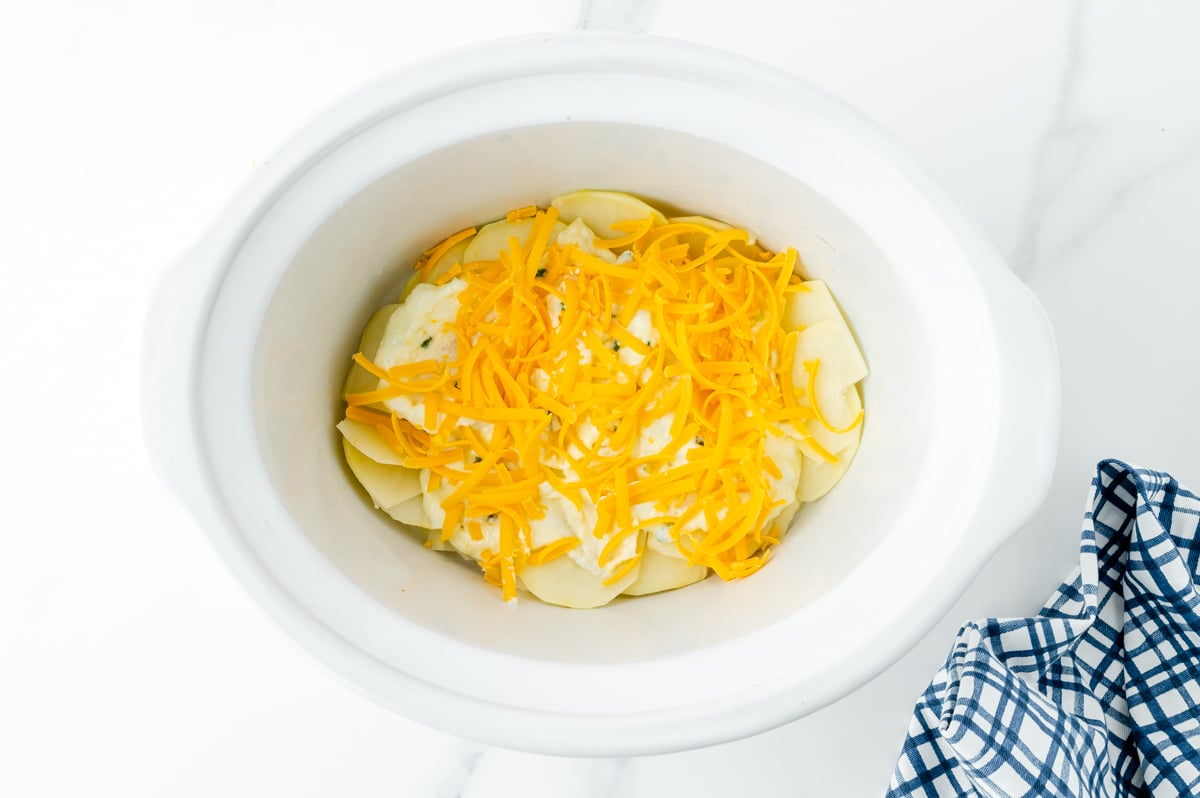 cheese sprinkled on top of potatoes in slow cooker