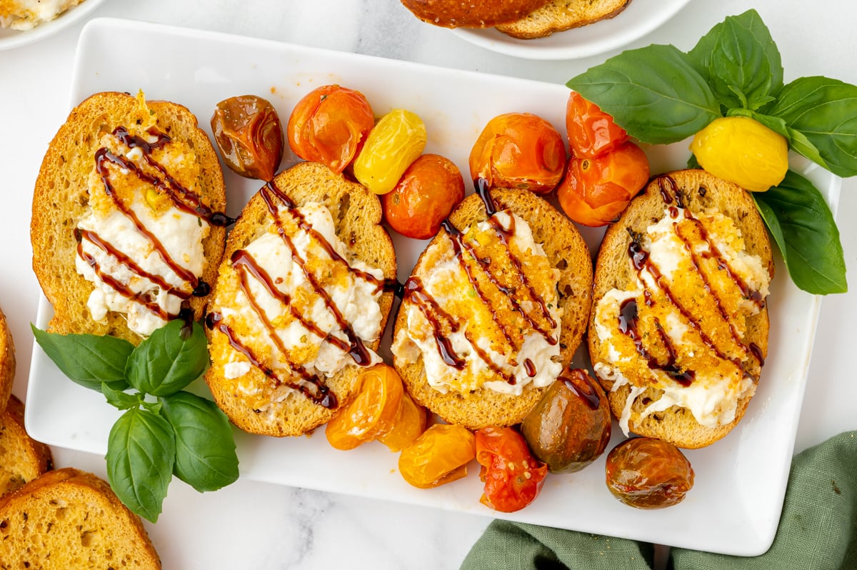 overhead shot of air fryer burrata spread onto four toasts with balsamic drizzled on top