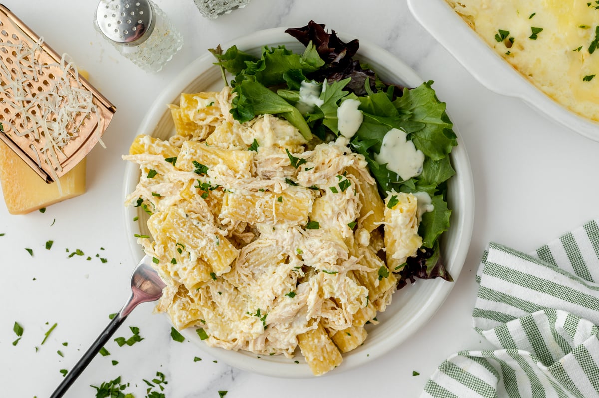 fork in chicken alfredo on plate with salad