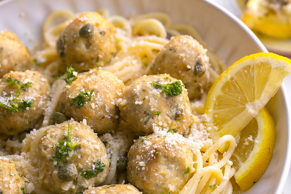 close up angled shot of chicken piccata meatballs over pasta