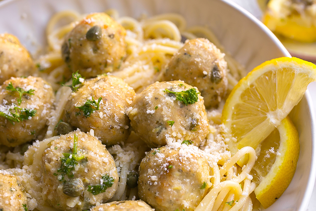 close up angled shot of chicken piccata meatballs over pasta