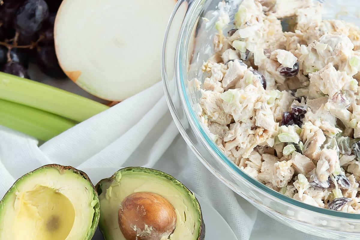 Chicken salad in a mixing bowl next to avocados