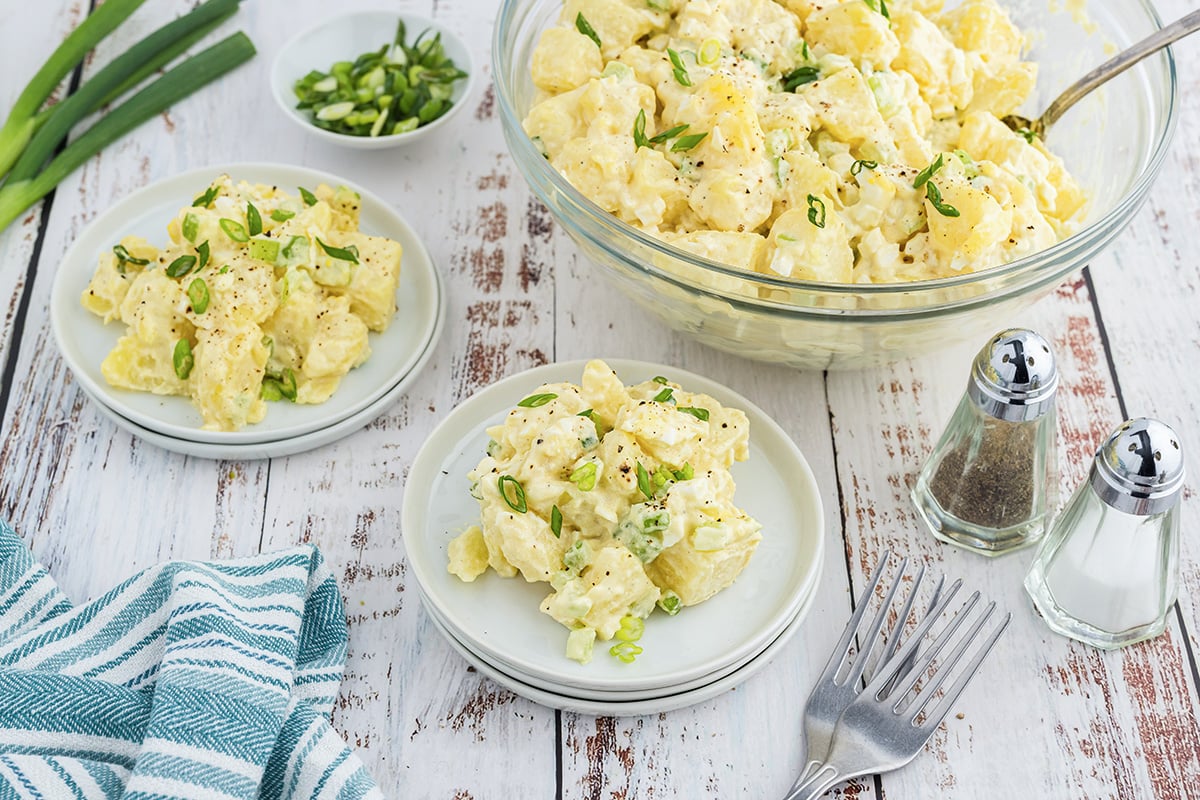 angled shot of classic potato salad in bowl and on plates