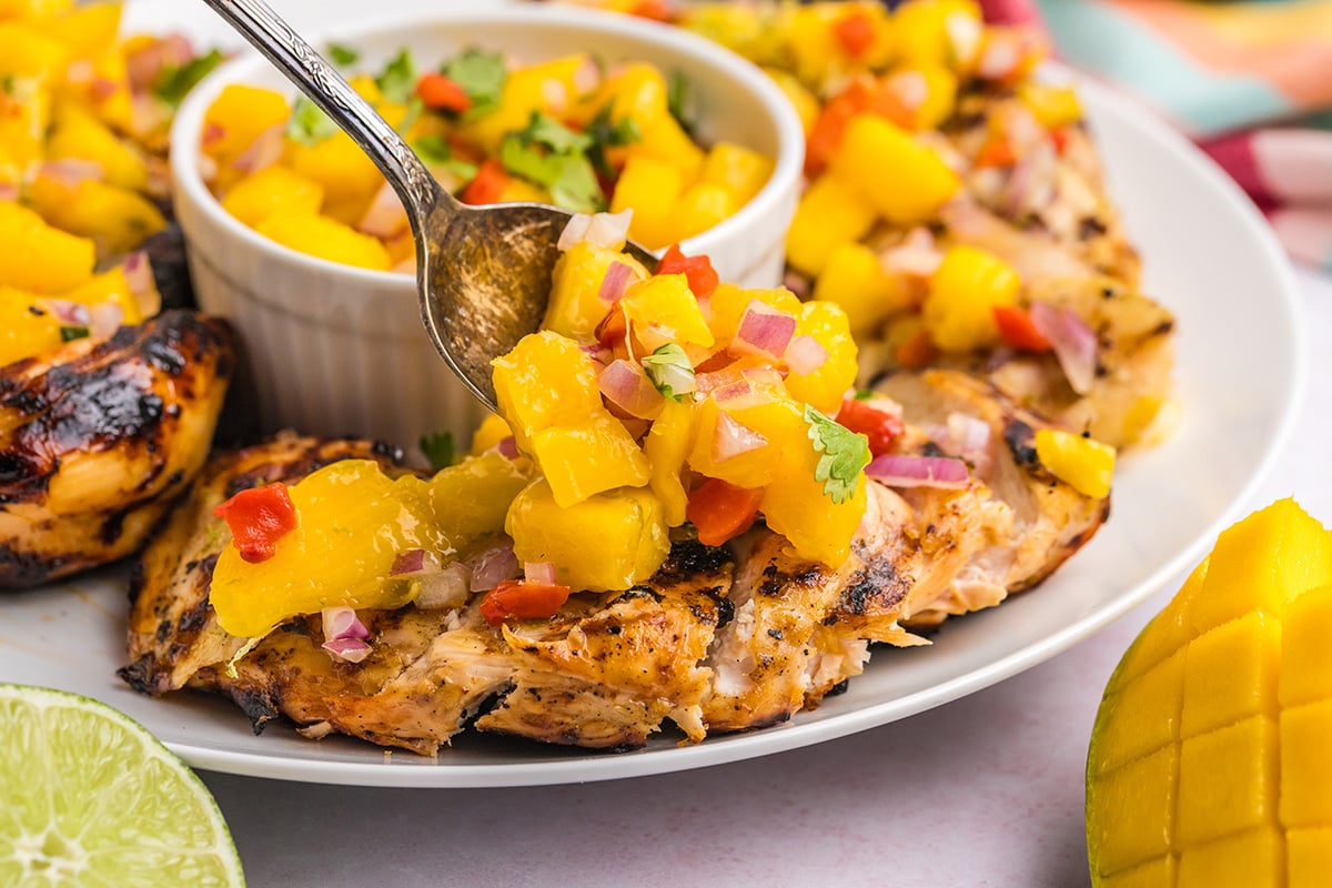 close up shot of spoon adding mango salsa to chicken