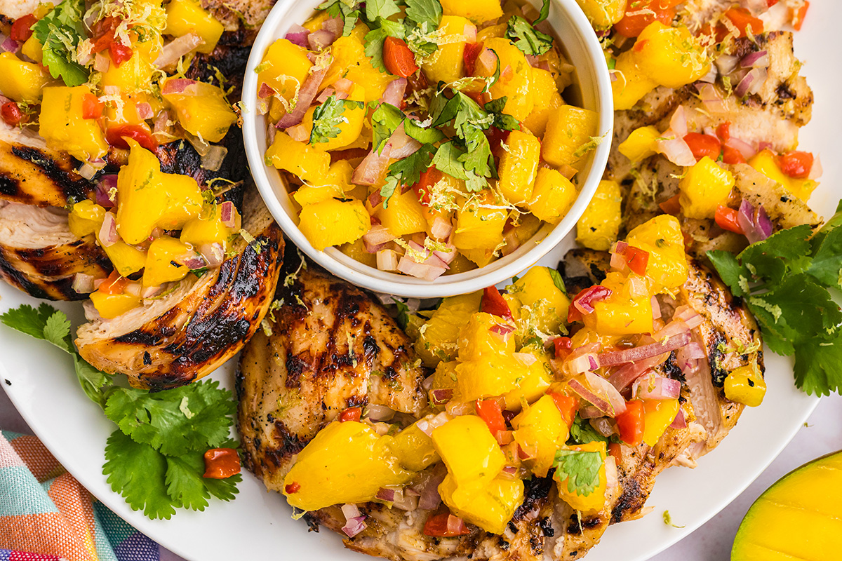 close up overhead shot of bowl of mango salsa surrounded by grilled chicken