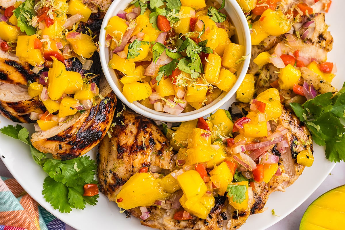 close up overhead shot of bowl of mango salsa surrounded by grilled chicken