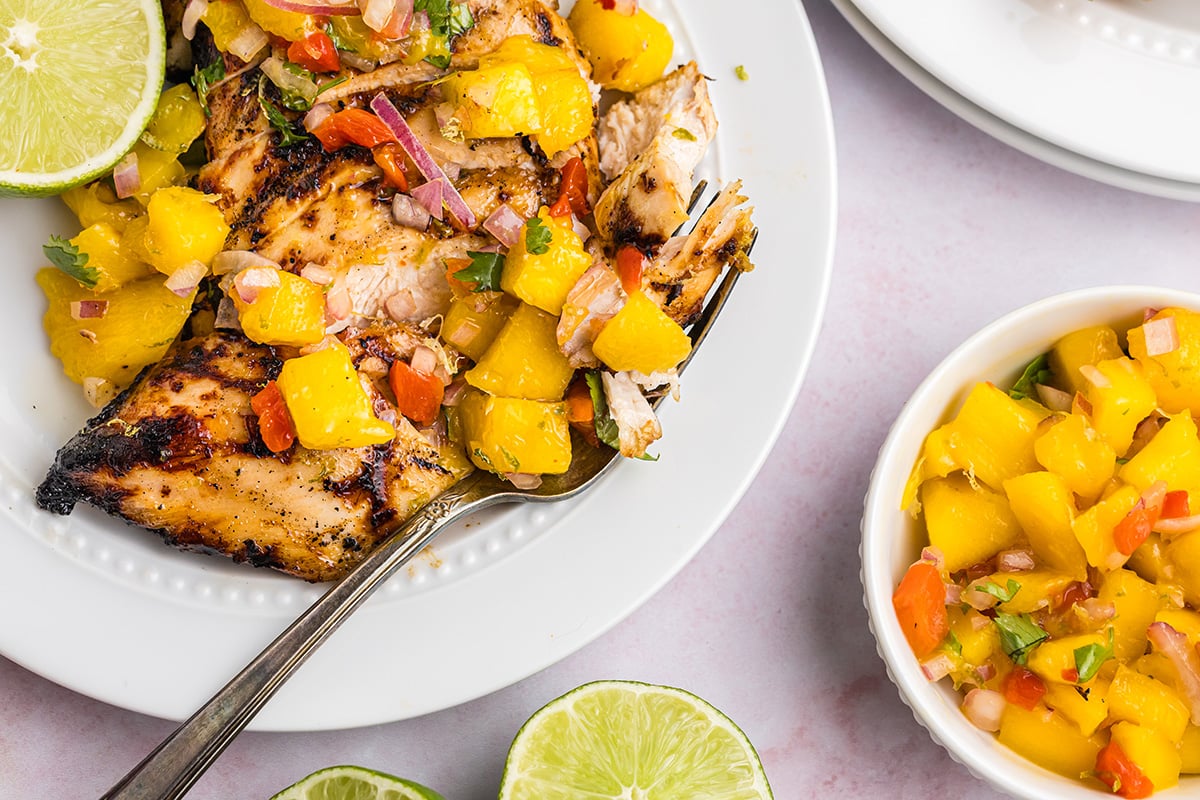 overhead shot of fork digging into grilled chicken with mango salsa 
