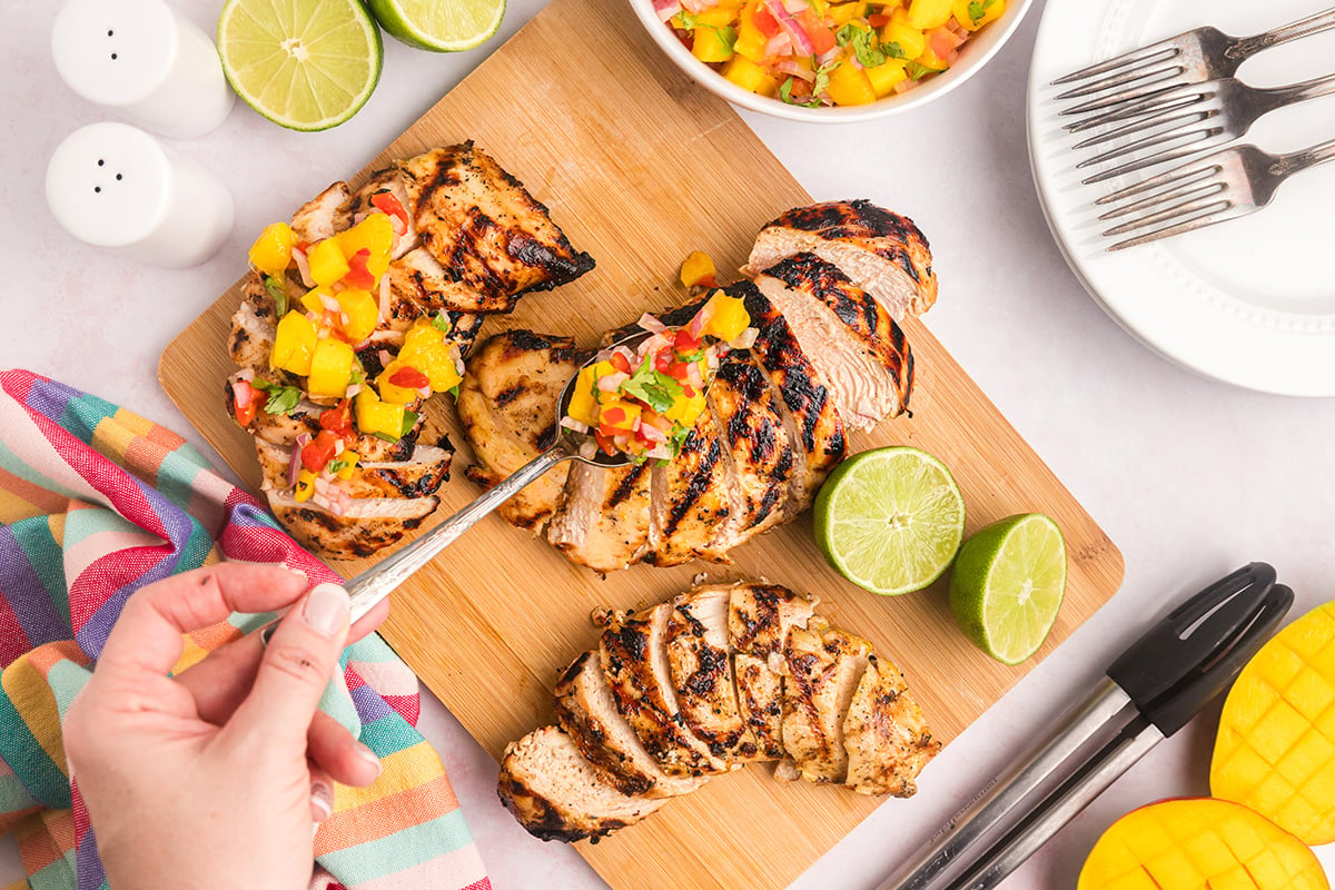 overhead shot of spoon adding mango salsa to chicken