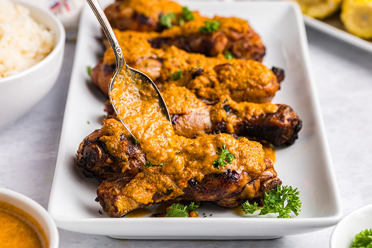 spoon adding sauce to tray of peri peri chicken