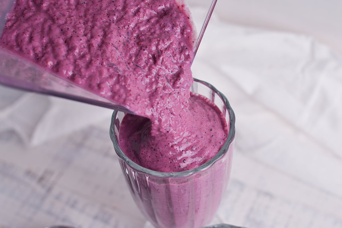 angled shot of grimace shake pouring out of blender into milkshake glass