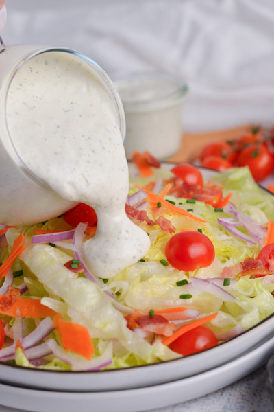straight on shot of light ranch dressing pouring onto salad