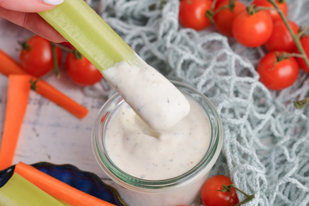 celery stick dipping into jar of healthy ranch sauce