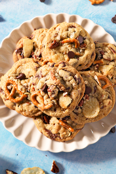 overhead scalloped plate of kitchen sink cookies with pretzels, chocolate chips and potato chips sticking out.