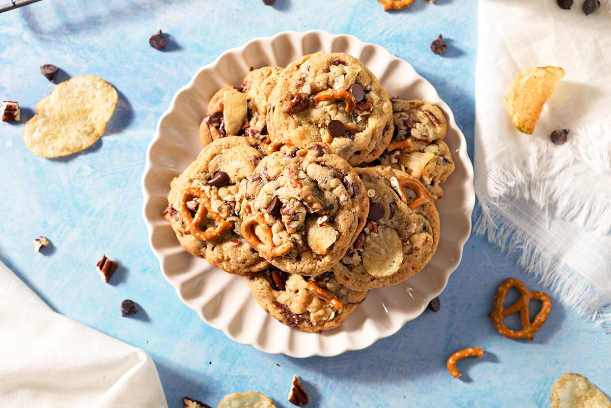 overhead scalloped plate of kitchen sink cookies with pretzels, chocolate chips and potato chips sticking out.