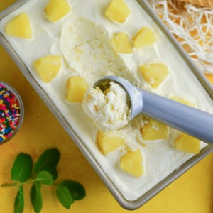 overhead of ice cream scooper in a pineapple ice cream recipe on yellow background