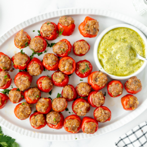 overhead shot of platter of sausage stiffed cherry peppers with bowl of green sauce