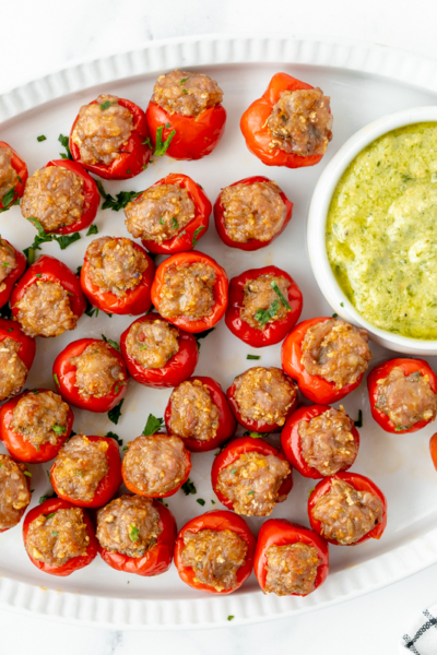 overhead shot of platter of sausage stiffed cherry peppers with bowl of green sauce